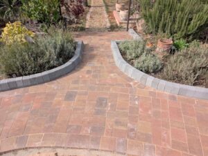 Block paving junction with curved grey edging between garden borders